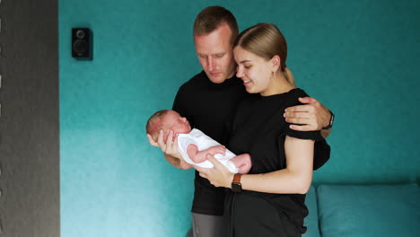 loving caucasian couple with their newborn child. mom looks at her baby with affection and dad strokes kid's head.