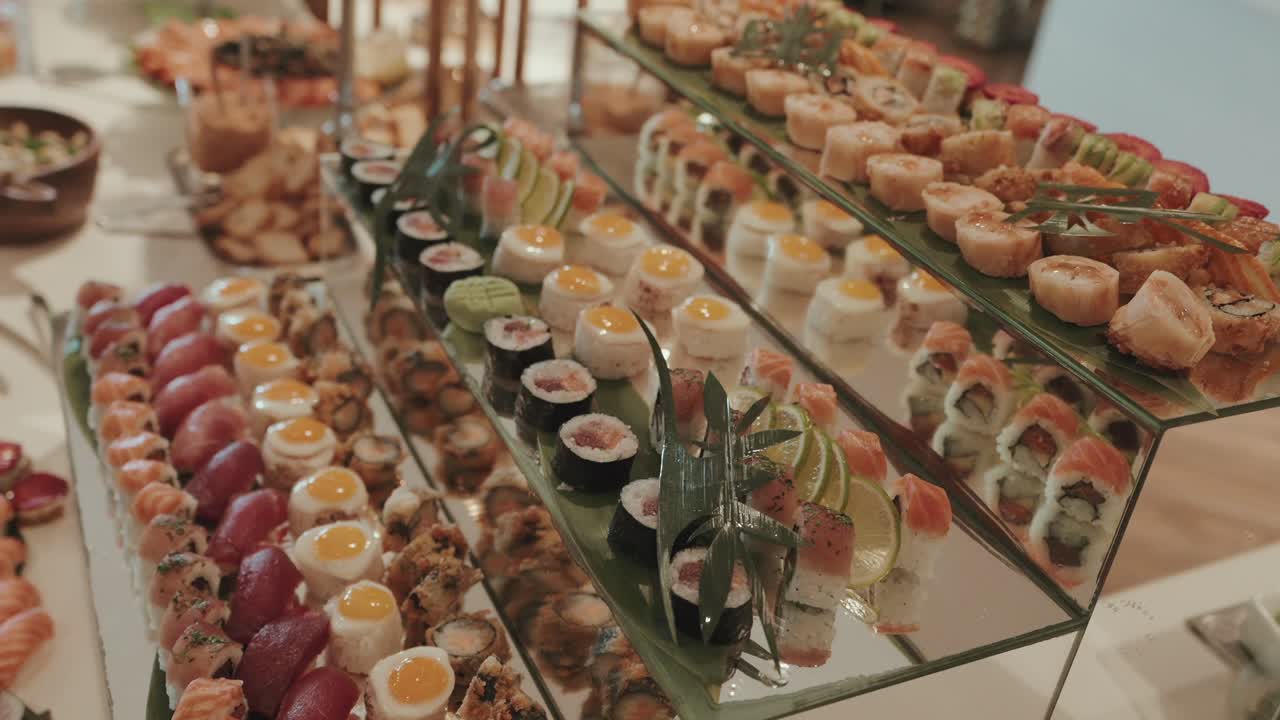 assorted sushi rolls and appetizers arranged on mirrored tiers at upscale buffet table