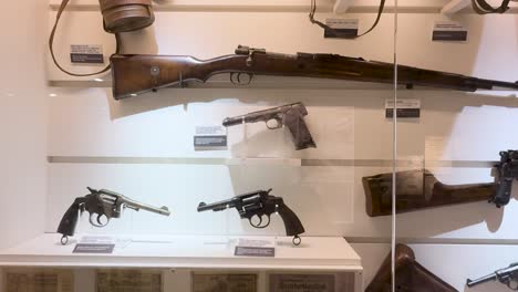 camera pans across museum case displaying labeled world war ii rifles, pistols, and revolvers