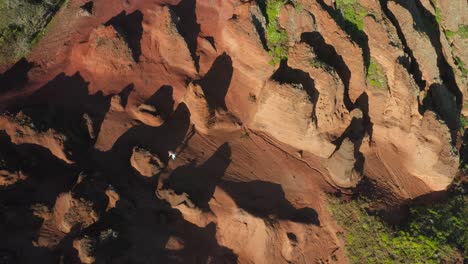 Woman-hiking-through-wild-rugged-mars-like-terrain-up-hill,-Ponta-do-Bode,-aerial