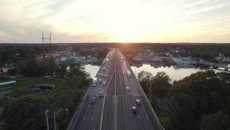 descending drone shot over interstate median at rush hour, traffic flow with bridge at golden hour