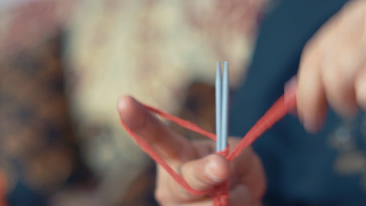 빨간 양모로 스카프의 첫 번째 행을 뜨개질하는 여자의 닫습니다