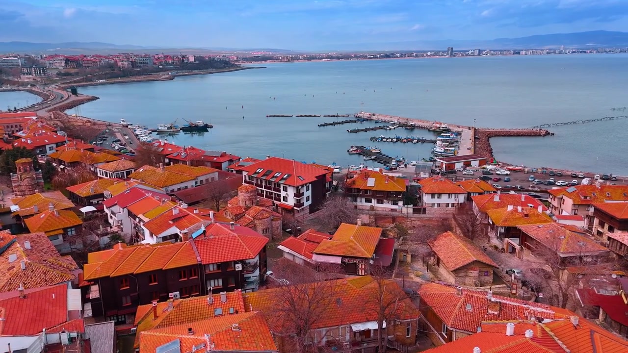 Vista dall'alto del porto e dei tetti rossi della città di Nessebar. Panorama aereo di case tradizionali con tetti rossi che si affacciano su una piccola baia marina con barche da pesca ormeggiate.