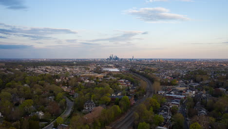 Aerial-drone-timelapse-of-the-Philadelphia-skyline-with-blue-skies-from-the-suburbs-over-green-summer-trees-and-Septa-train-tracks