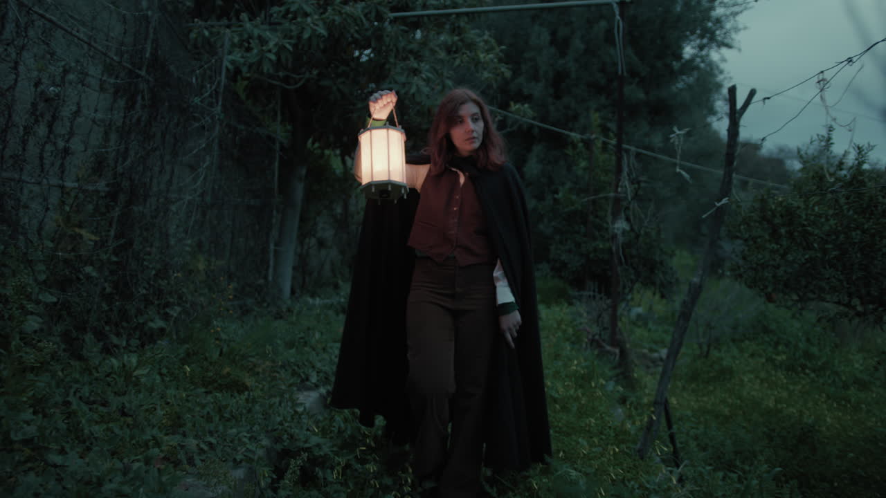 una mujer misteriosa camina entre los árboles para un rito religioso en una casa abandonada por la noche.