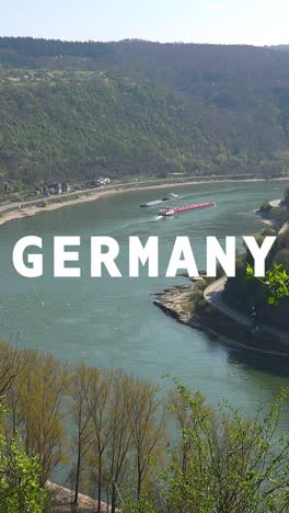 Vertical-Video-Aerial-Drone-Shot-Of-River-With-Cargo-Boats-With-Animated-Graphic-Spelling-Out-Germany