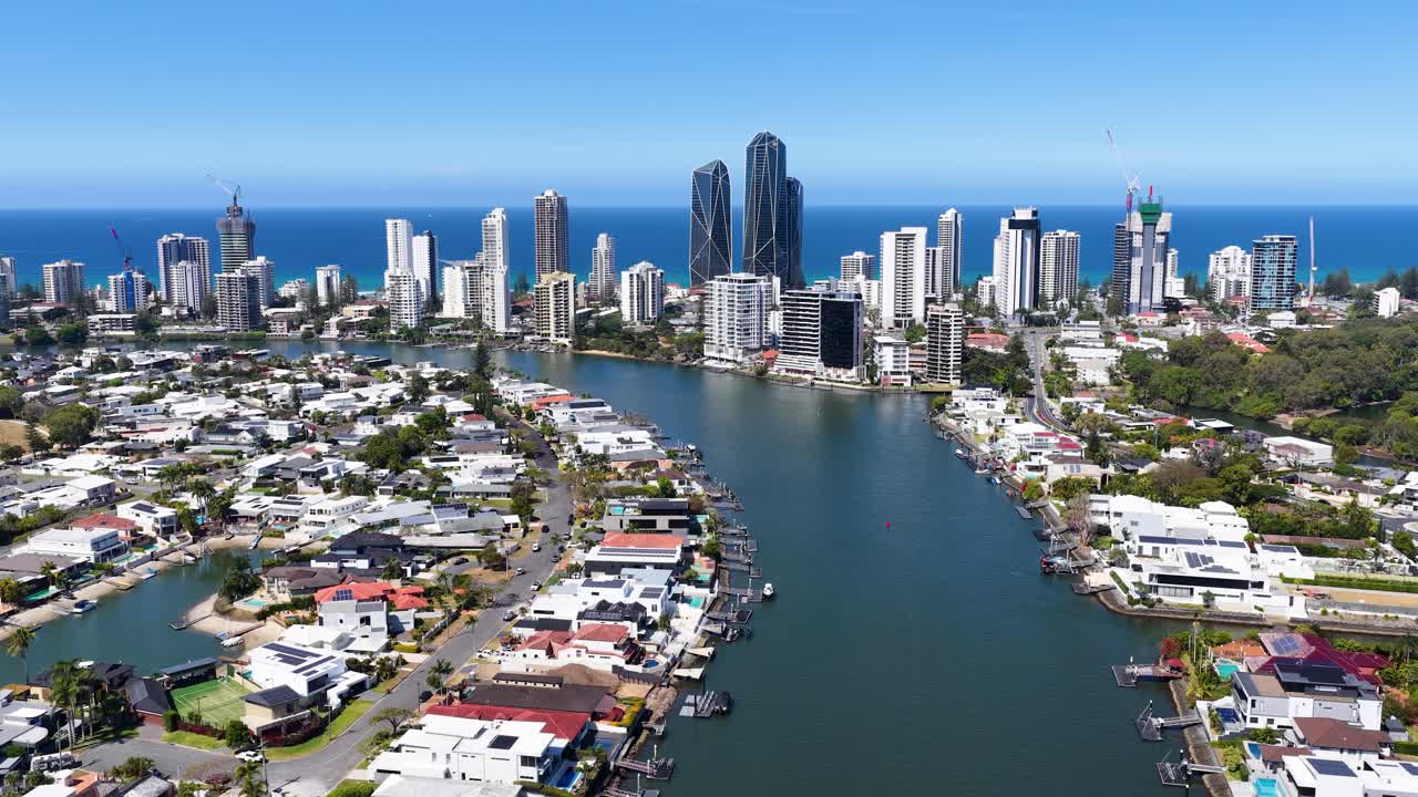 Daytime drone footage glides above river, residential homes, and skyscrapers near Gold Coast coastline