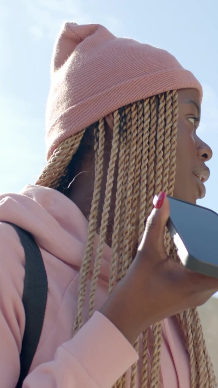 Video verticale: Donna che parla, tiene in mano un telefono, si gira verso lo skyline, con un berretto rosa, spazio per il testo.