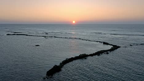 Aerial-flyover-tranquil-ocean-water-with-outstanding-rocks-and-golden-falling-sunset-at-horizon