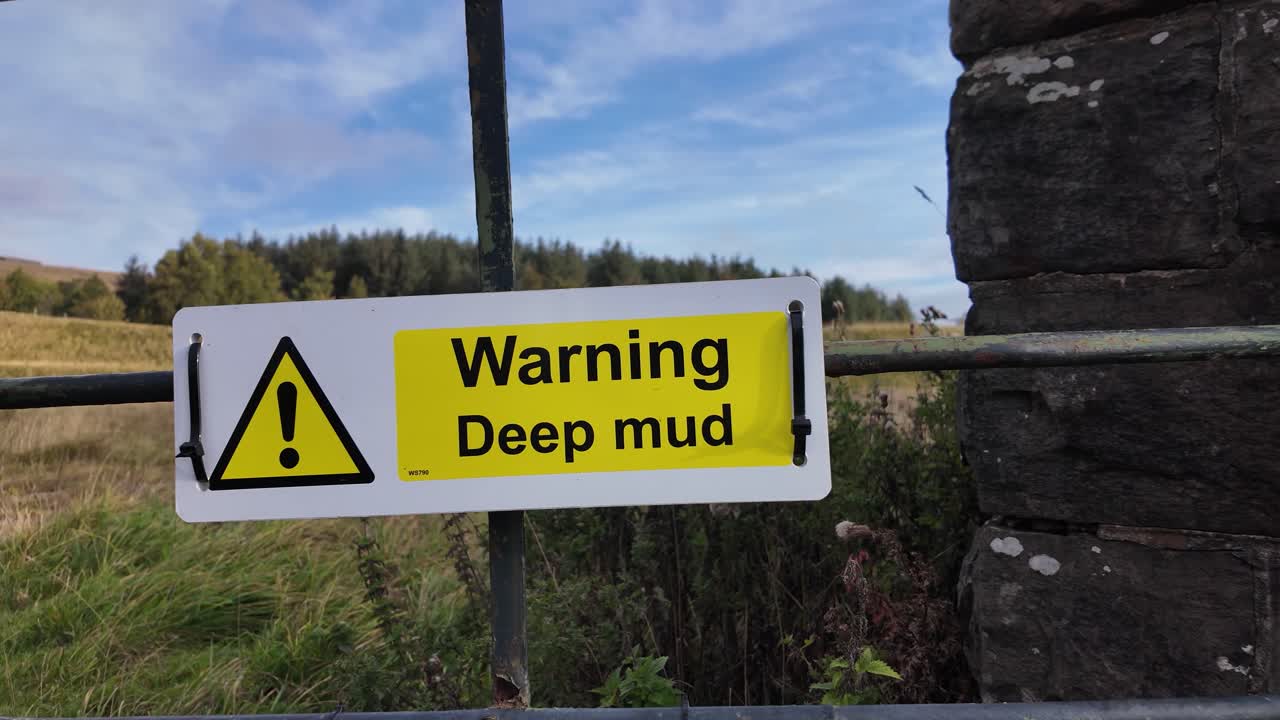 Yellow sign displaying a warning for deep mud on a metal farm gate