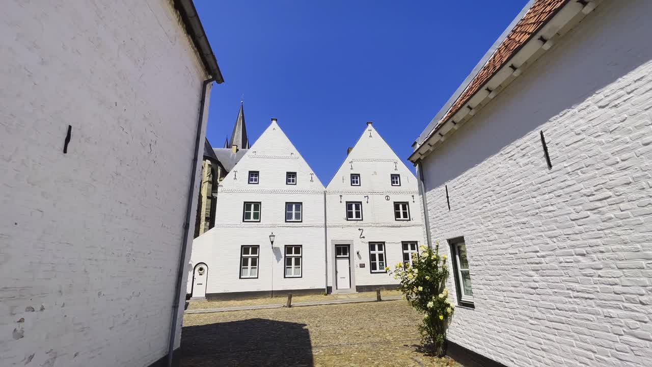Static shot of the pure white building Hofstraat in Thorn, Limburg with a view of the dutch architecture as cyclists pass by on a sunny day