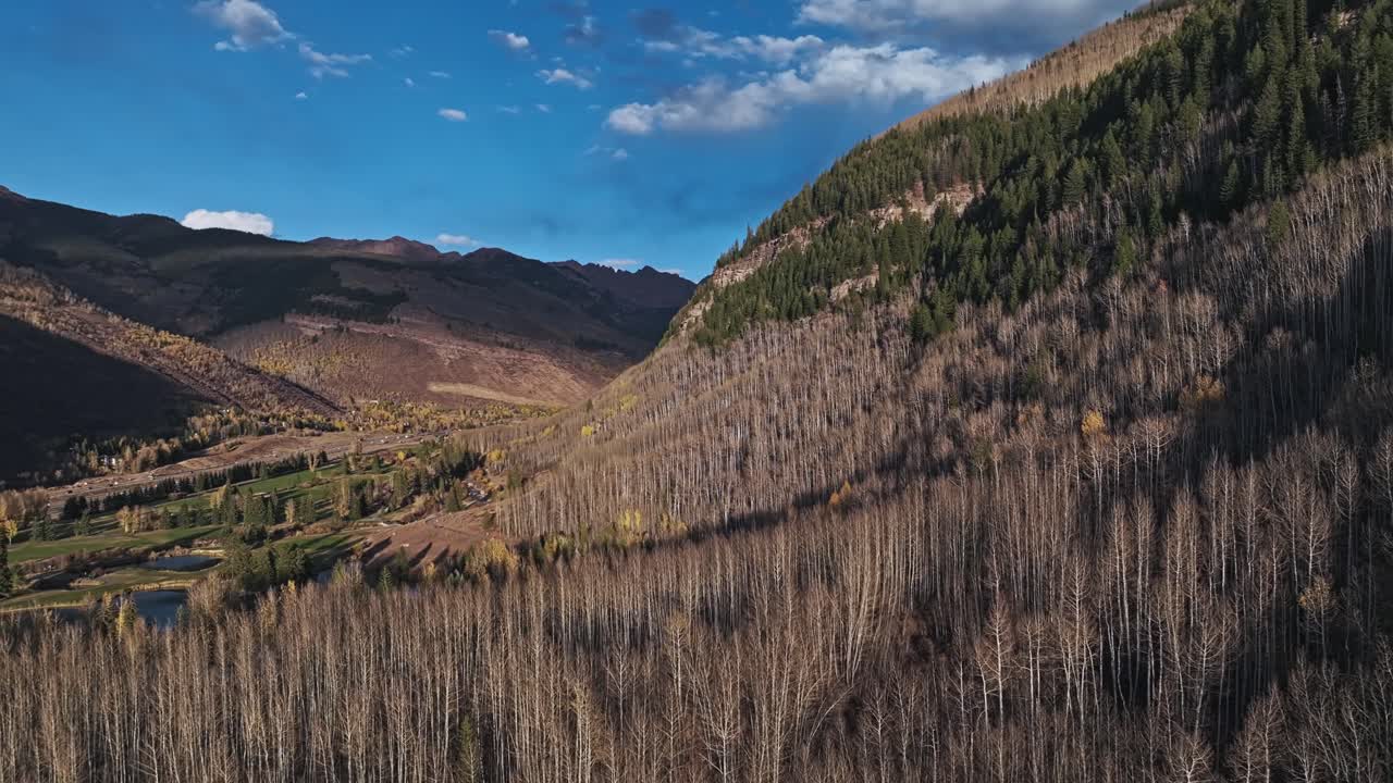 Serene golf course surrounded by Vail's mountains, with bare and evergreen trees and rugged cliffs beyond