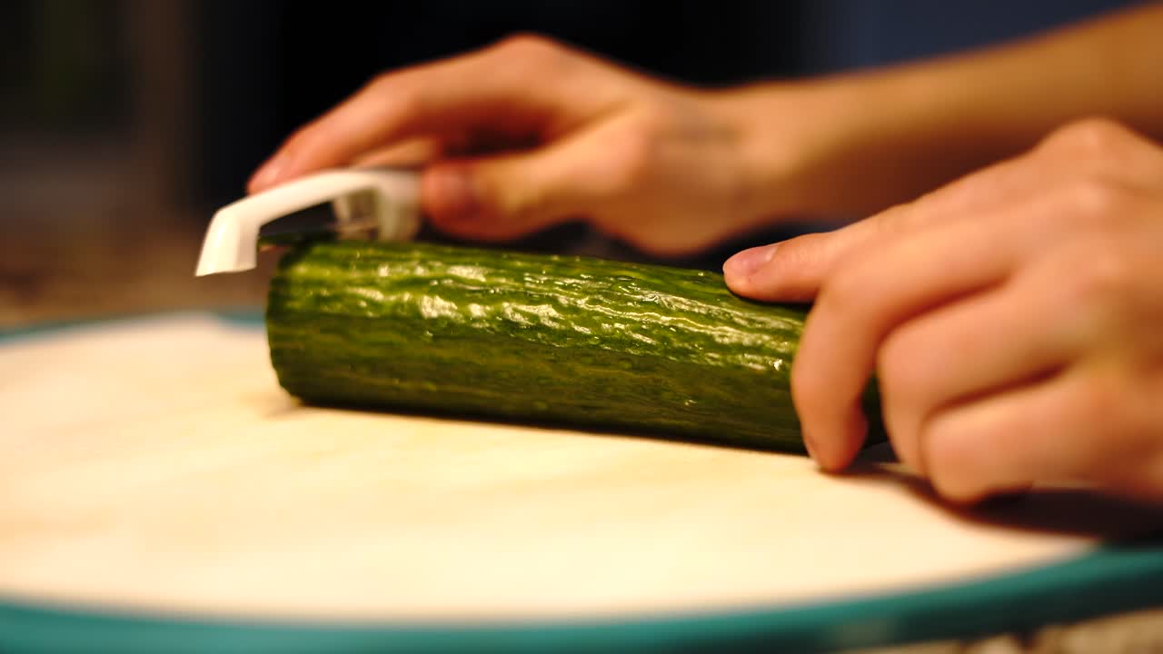 Person slowly peeling nutritious cucumber with vegetable scraper, home kitchen