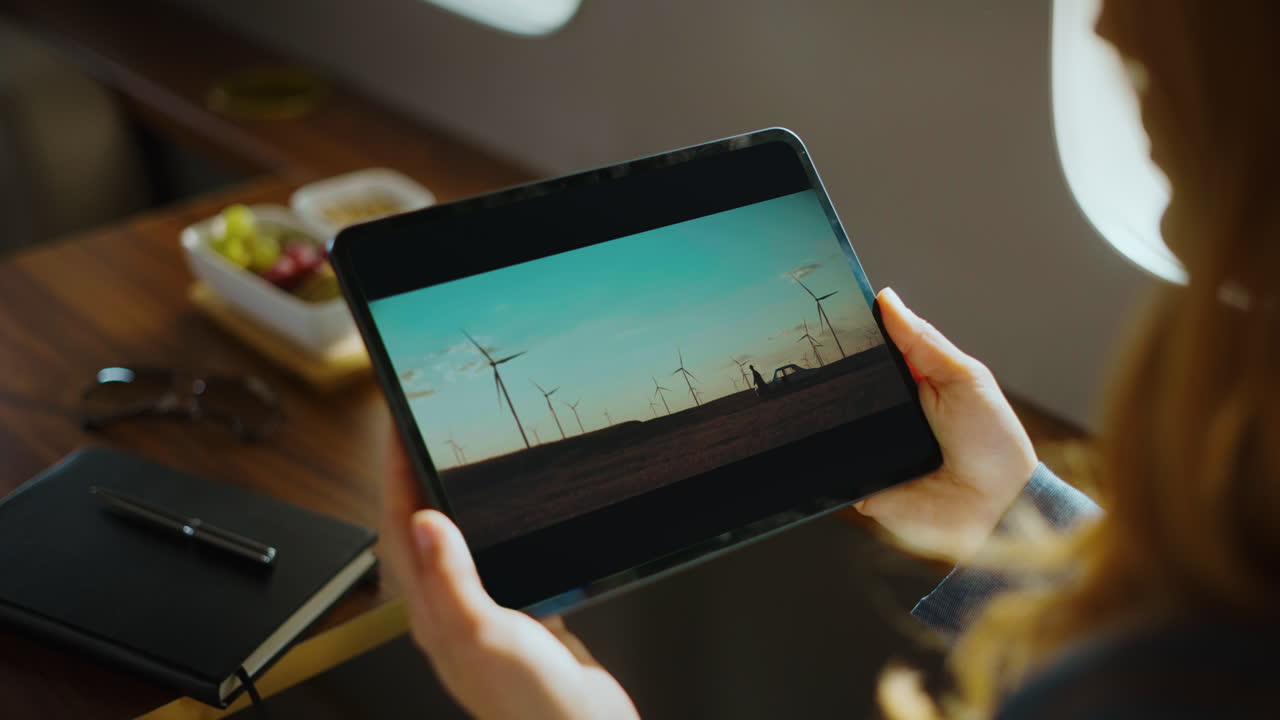 Woman using tablet inside private jet viewing wind turbine images