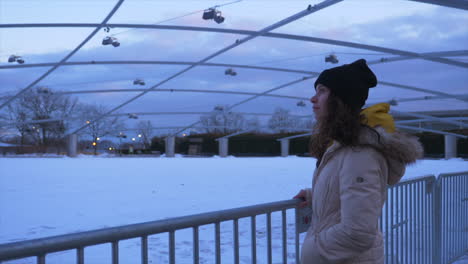 a young woman looks around in the cold behind a gate in wonder at the snow and sky in an outdoor structure public park,