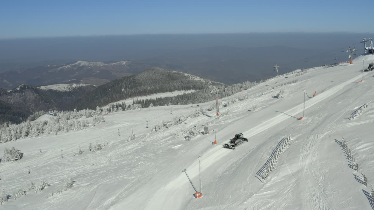 Gatto delle nevi in azione su una pista da sci in un paesaggio montano invernale.