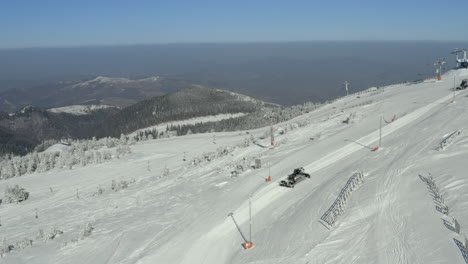 snow groomer working on a ski slope in a winter mountain landscape