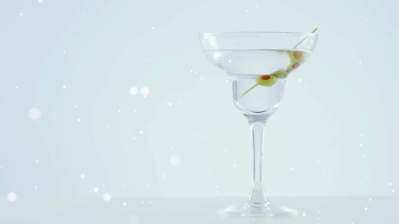 Macchie bianche che fluttuano su olive che cadono in un bicchiere da cocktail su sfondo grigio