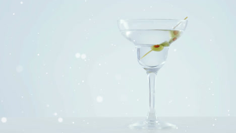 white spots floating over olives falling into cocktail glass against grey background