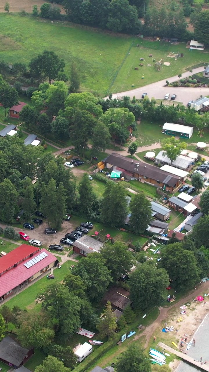 Ripresa cinematografica dall'alto di un resort turistico con cabine in legno, area parcheggio e accesso alla spiaggia nella pittoresca regione della Kaszuby. Adatto per il marketing turistico.