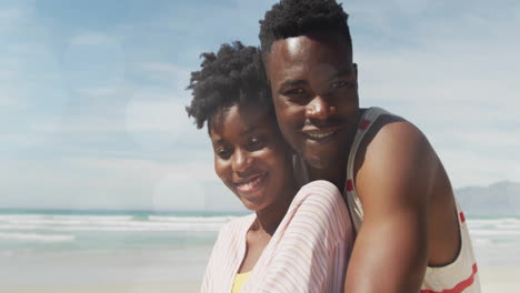 couple hugging on sandy beach with ocean waves, showing floating business icons and chart overlays