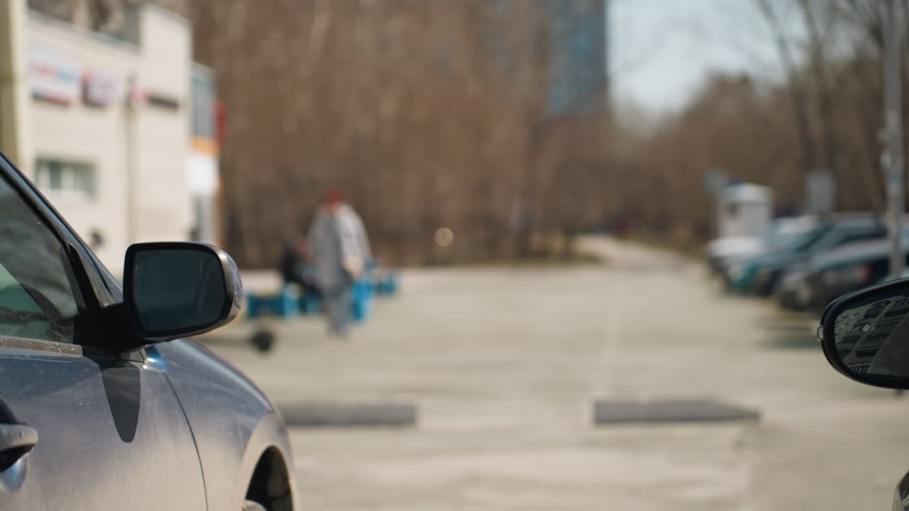 Close view of budding tree branches in an urban parking lot with city buildings in the background, with a bokeh view of someone coming