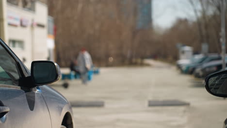 close view of budding tree branches in an urban parking lot with city buildings in the background, with a bokeh view of someone coming