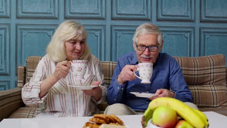 Mature-family-couple-grandfather,-grandmother-relaxing-on-cozy-sofa-enjoying-conversation-at-home