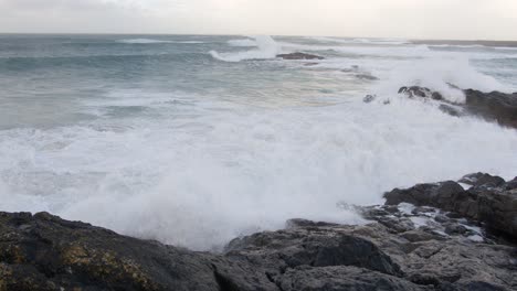 slow motion shot of large, breaking waves crashing over the cliffside during a storm in the bay by tangasdale beach, near castlebay on the isle of barra