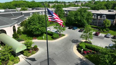 Drone-view-zooming-in-on-a-large-apartment-community,-focusing-on-the-American-flag-flowing-in-a-light-breeze