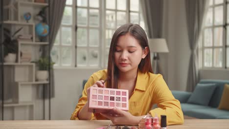 Vlogger Asian Female Showing Eye Shadow Palette. Beauty Blogger Woman Make-Up Routine Tutorial. Influencer Girl Live Streaming Cosmetics Product Review In Home Studio