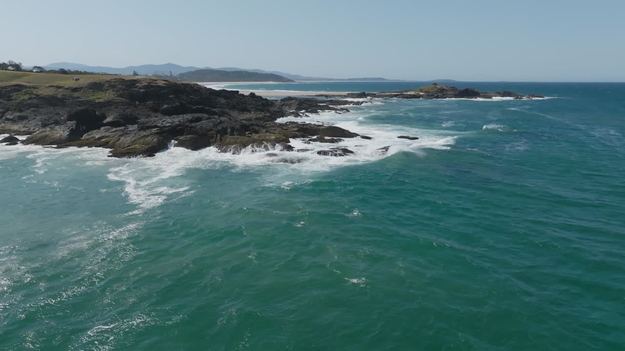 Drone aerial clip showing waves crashing onto rocky shoreline and pod of dolphins swimming close to rocks