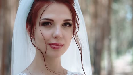 portrait of a bride in a forest in a wedding dress that touches a curl of her hair smiling close-up slow motion