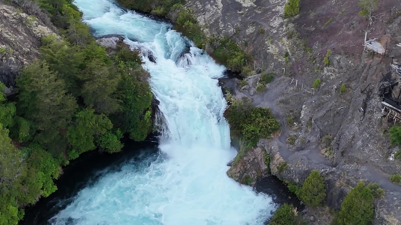 Aerial cinematic footage of Truful Truful River waterfall flowing through volcanic canyon surrounded by dense green forest. Multiple cascades drop through ancient lava formations in Conguillio...