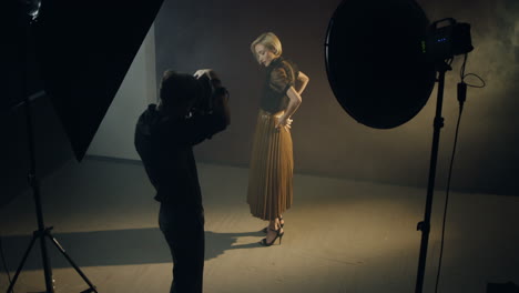 vista de ángulo alto de la joven modelo caucásica posando en el estudio oscuro mientras el fotógrafo toma fotos de ella