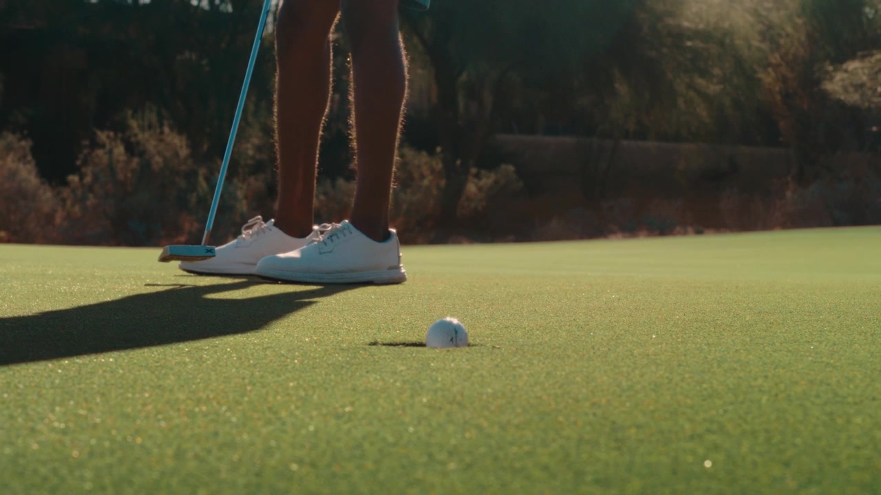 Golfista proměňuje deseti stopý putt s protisvětlem a sluneční září na pouštním greenu ve zpomaleném záběru, skvělé pro golfové promo akce, vítězné okamžiky a sportovní marketing.