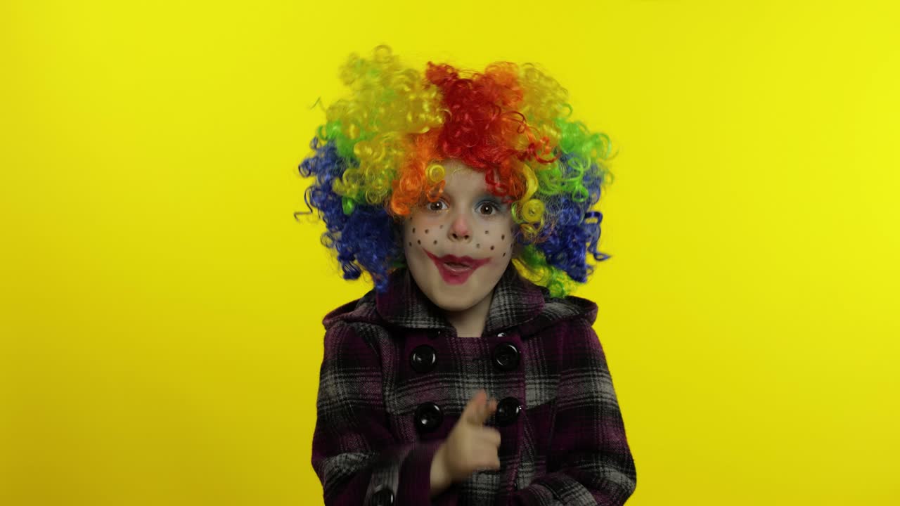 una pequeña niña payasa con una peluca colorida haciendo caras tontas, divirtiéndose, sonriendo, bailando. halloween