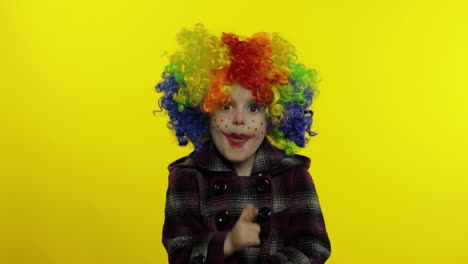 una pequeña niña payasa con una peluca colorida haciendo caras tontas, divirtiéndose, sonriendo, bailando. halloween