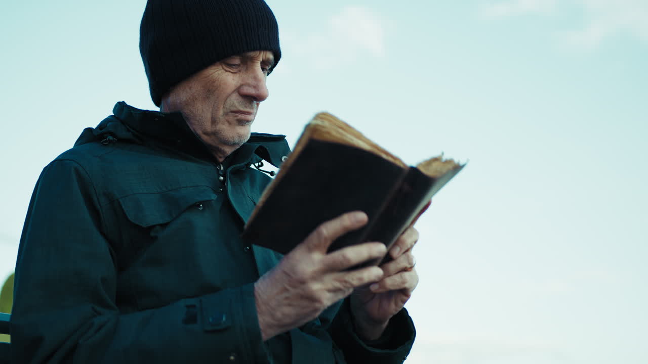 Elderly Man Carefully Reading an Old Book Outdoors
