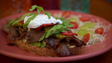 Slow-motion-panning-of-a-beef-deli-sandwich-topped-with-arugula-mozzarella-cheese-pickles-cucumber-and-tomato-served-with-salad