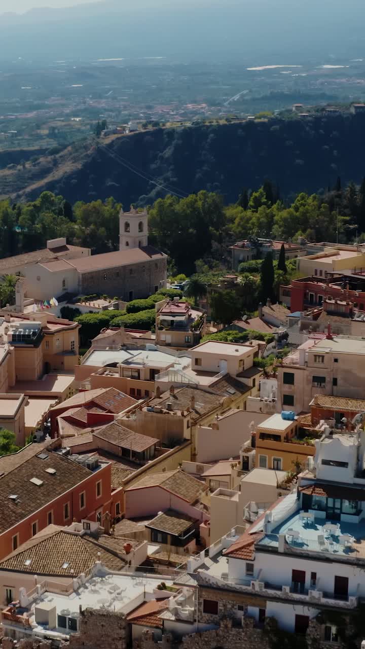 vertical aerial de volar sobre los tejados en la ciudad italiana en las montañas con vistas a la costa del mar mediterráneo. ciudad histórica de taormina en sicilia. vistas impresionantes con terreno montañoso.