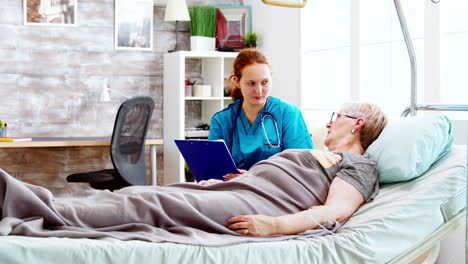 social worker consulting an elderly disabled woman who lies in hospital bed