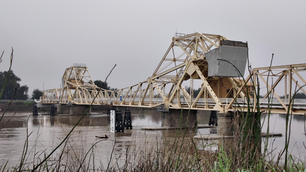 A smooth, professional dolly-in shot pushing forward toward a massive yellow metal truss bridge.