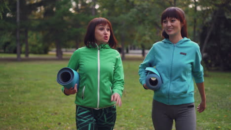 two women walking in a park with yoga mats