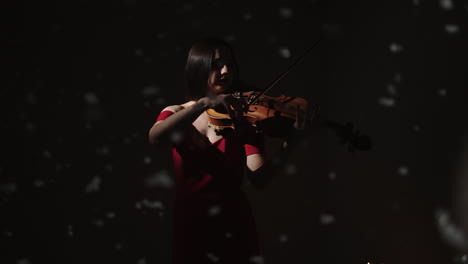 woman playing violin in a red dress under snowfall