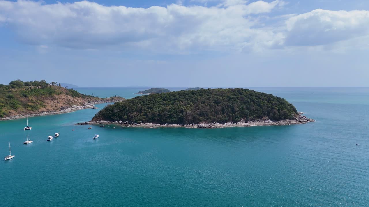 드론 영상은 태국 푸켓의 조용한 섬과 배를 포착하여 부분적으로 구름이 가득한 하늘 아래 푸른 물과 울창한 초록색을 보여줍니다.