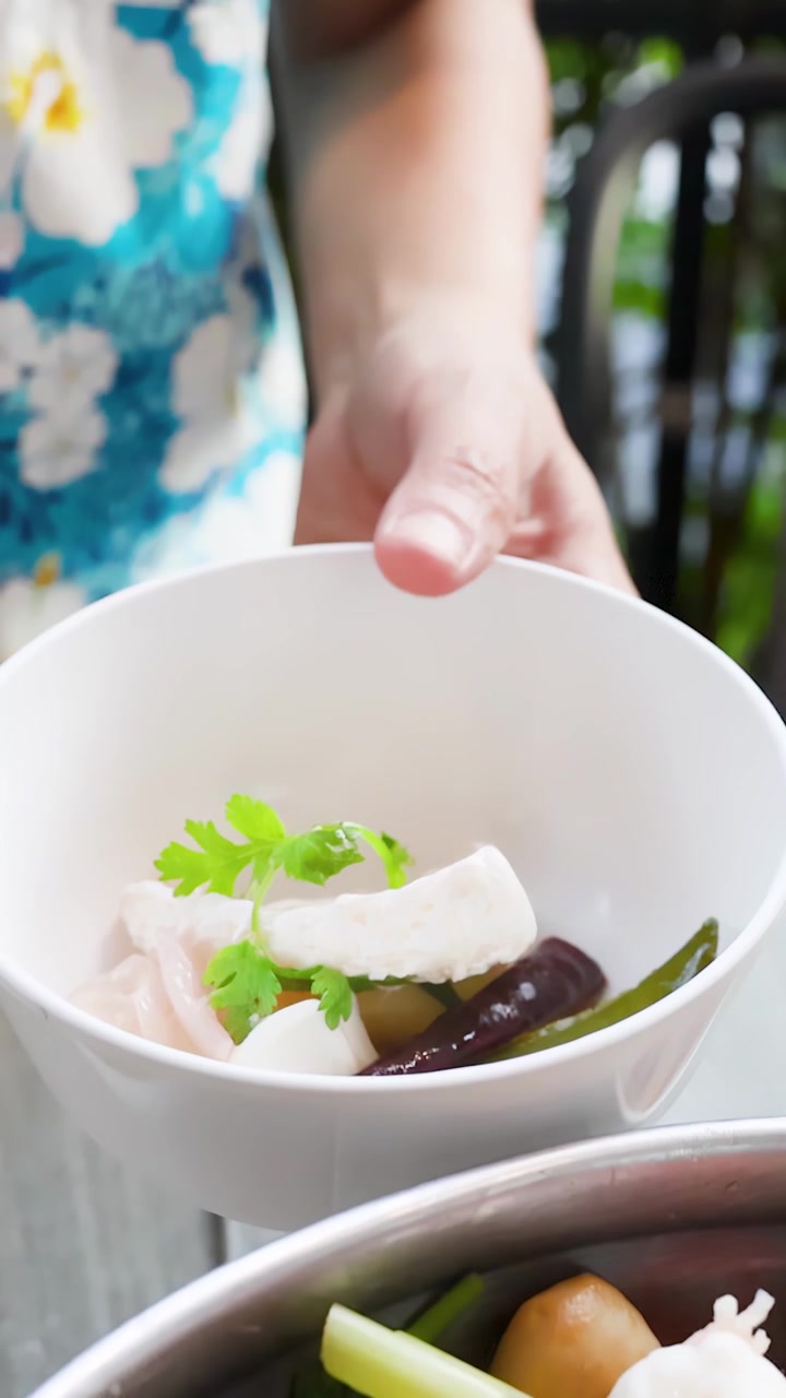 En person øser varm tom yum-suppe med reker og urter i en bolle utendørs