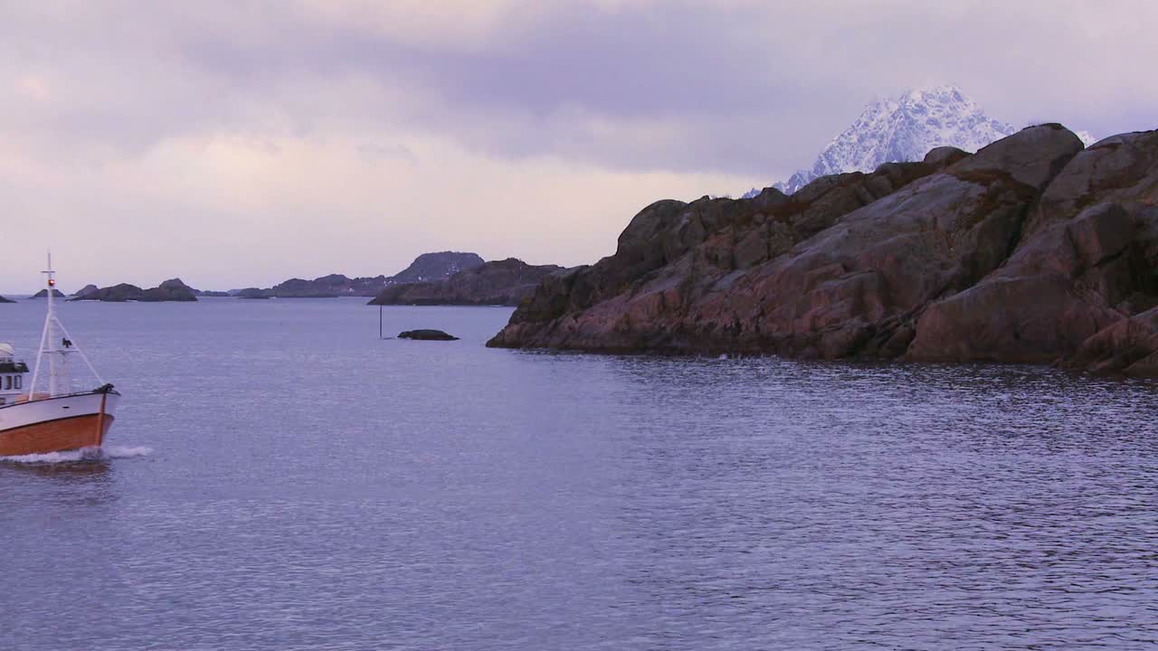 un barco de pesca se dirige a través de fiordos en el ártico en agua verde vidriosa en las islas lofoten noruega 4