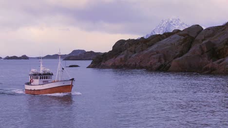 a fishing boat heads through fjords in the arctic on glassy green water in the lofoten islands norway 4