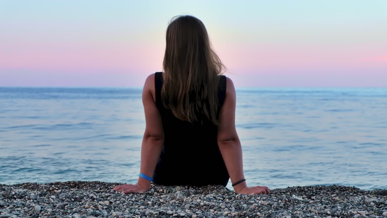 Una donna seduta sulla spiaggia al tramonto sulla costa del Mar Mediterraneo a Kemer, Turchia